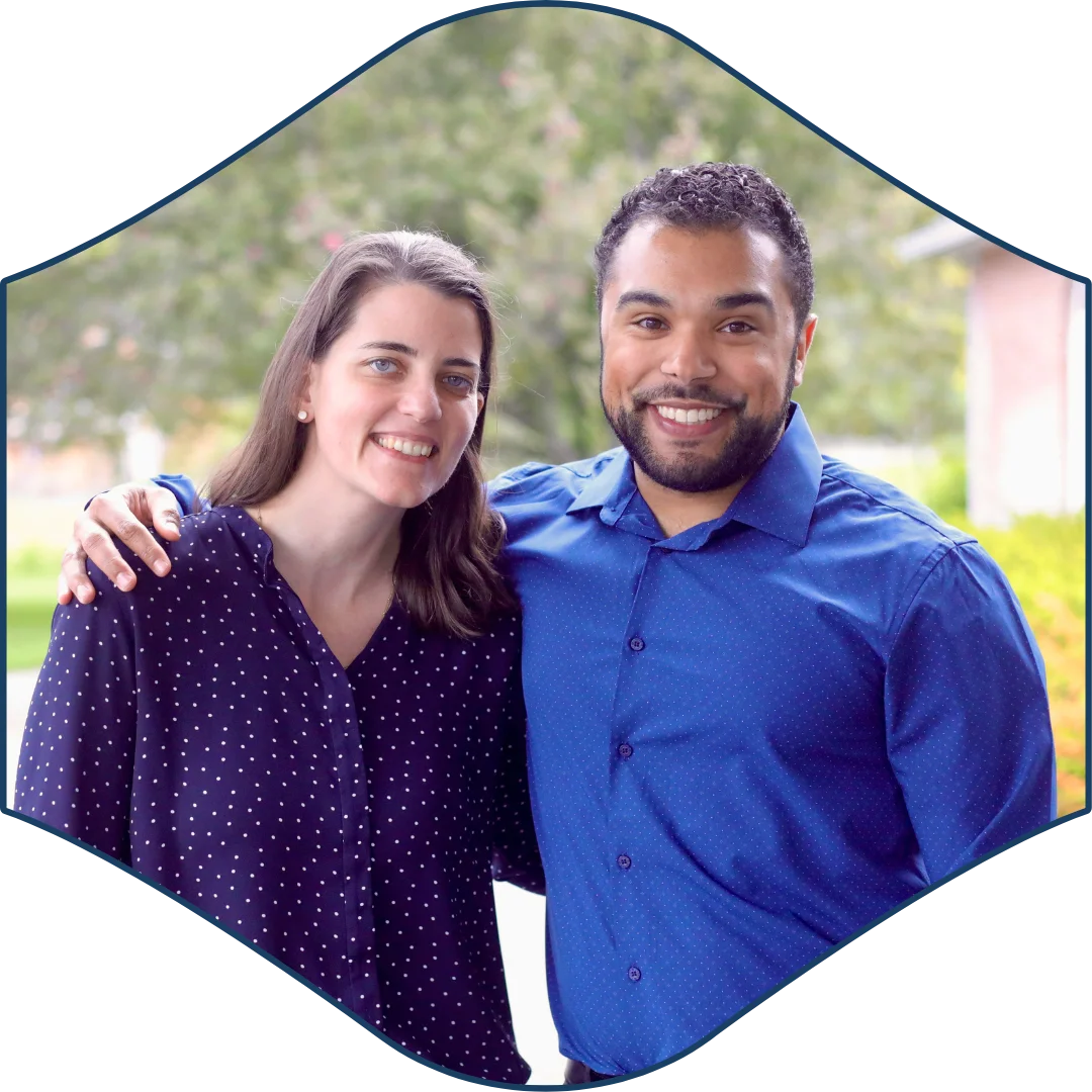 Smiling woman and man standing closely together outdoors, framed in a curved badge shape with a soft natural background.